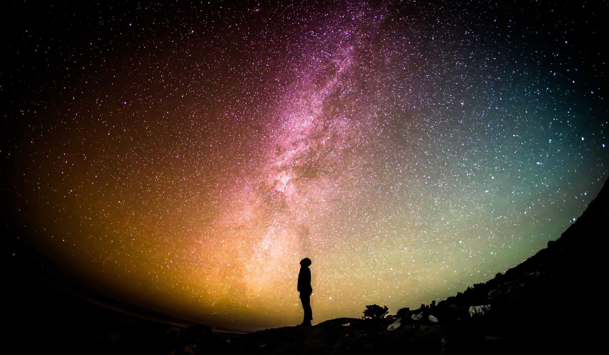 A single figure standing beneath the Milky Way on open ground